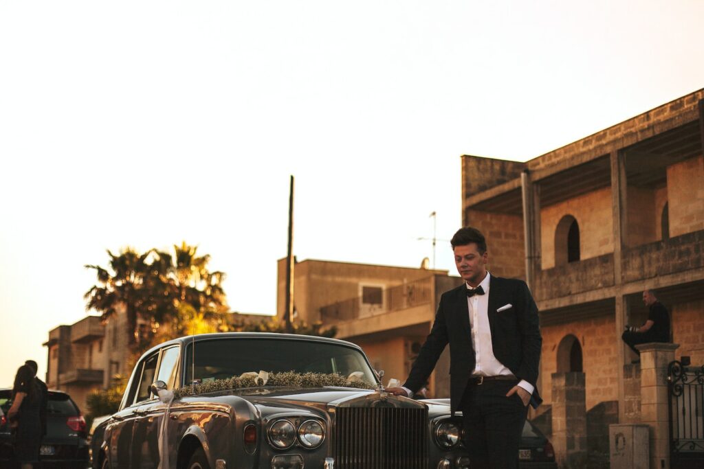 man wearing black suit jacket standing near gray car